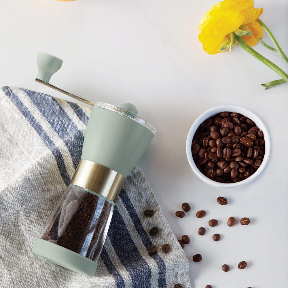 travel grinder next to a cup of coffee beans