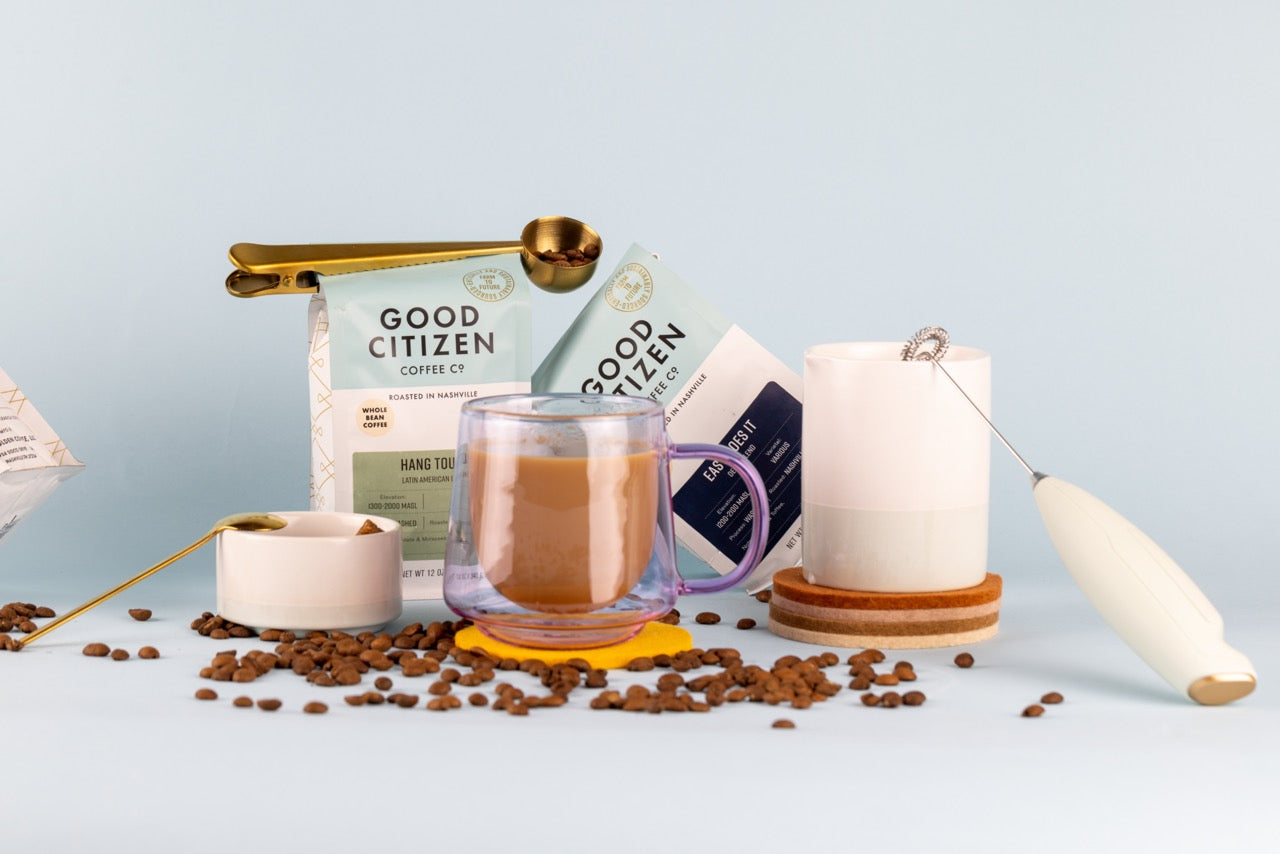 mug filled with coffee with a cream set and coffee bags surrounding with a frother