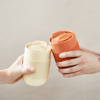 BUTTER YELLOW & TERRACOTTA CERAMIC TUMBLERS BEING HELD BY TWO PEOPLE